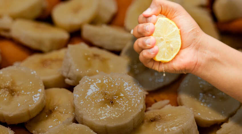 A hand squeezing a lemon into slices of bananas