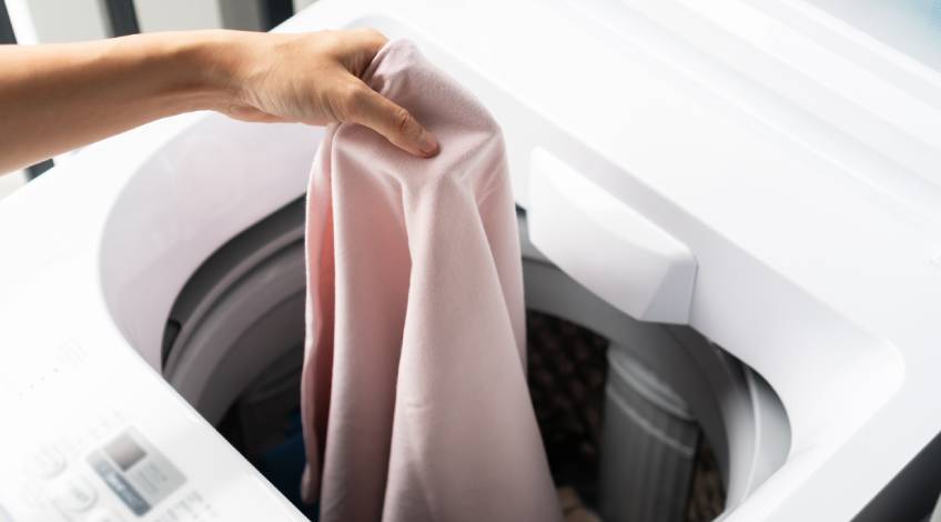 person placing clothes in a top load washing machine