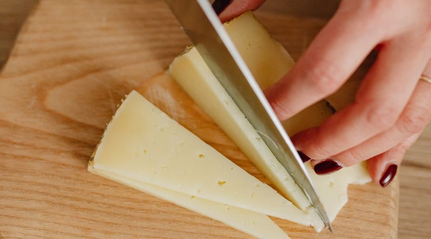person slicing cheddar cheese