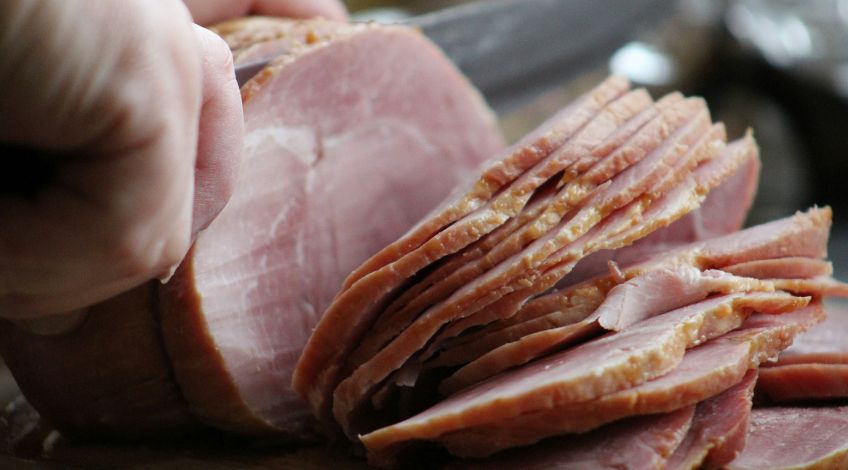 person slicing ham on a cutting board