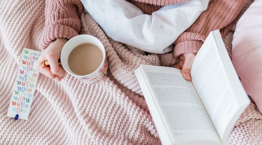 person reading in bed with cup of coffee